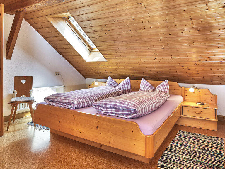 Ein gemütliches Bett steht in dem holzverkleideten Schlafzimmer ,in einer der Ferienwohnungen, auf dem Pfefferhof.